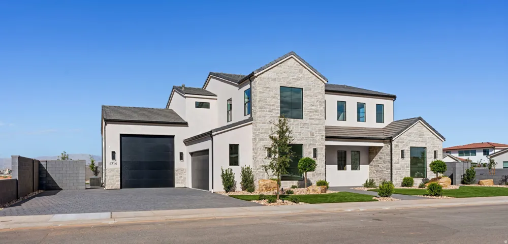 Modern stucco and stone-clad exterior with a dark-toned roof, RV Garage and paver driveway.