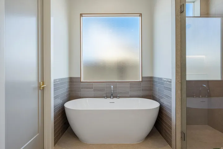 Freestanding soaking tub with chrome fixtures, frosted glass window, and subway tile wainscoting