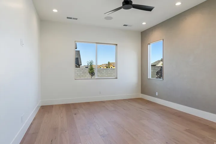 Primary Ensuite Bedroom has light-toned wood flooring, recessed ceiling lighting, three large windows, black ceiling fan, and a textured accent wall
