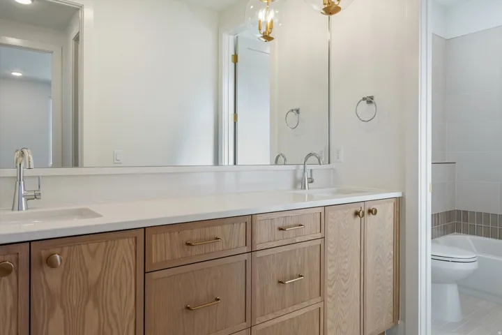 Dual vanity with wood-finish cabinetry and brass hardware, featuring integrated sinks and chrome faucets