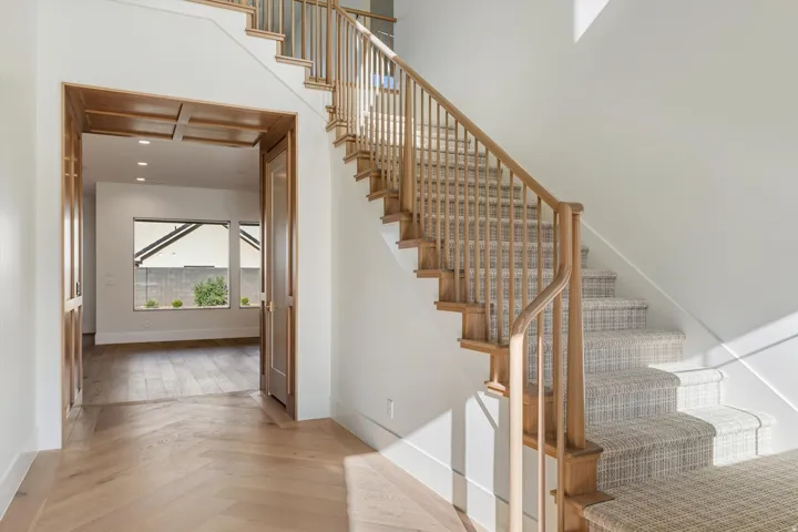 Herringbone wood flooring, wood-paneled doorway, recessed lighting, carpeted staircase, and wooden banister