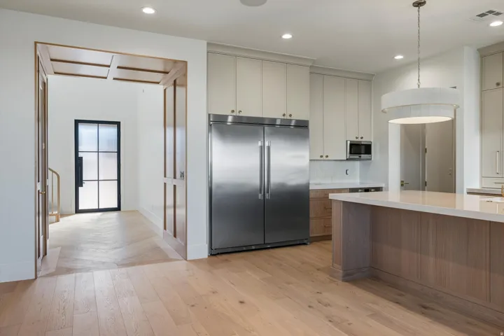 Gourmet kitchen with stainless steel refrigerator, white shaker cabinetry, and a large island with a light-toned quartz countertops