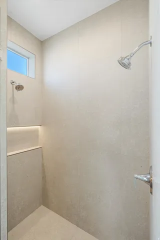 Tiled shower with dual shower heads, built-in recessed shelf with accent lighting, and transom window