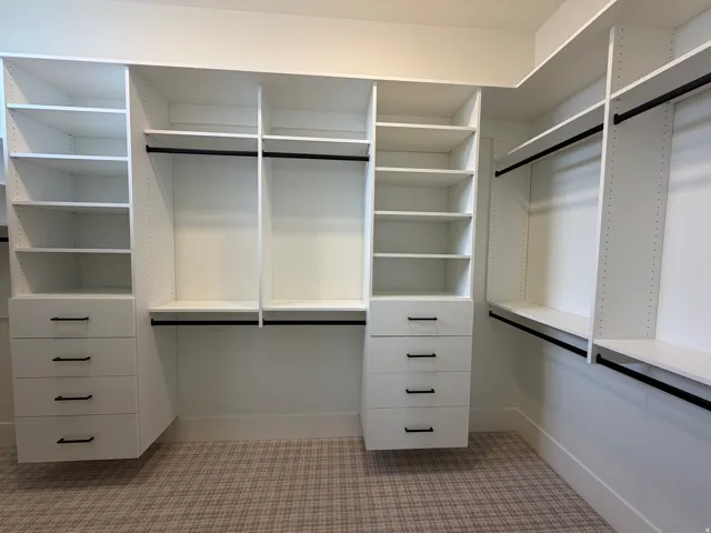 Built-in white custom closet system featuring multiple shelving units, hanging rods, and integrated drawers with black hardware