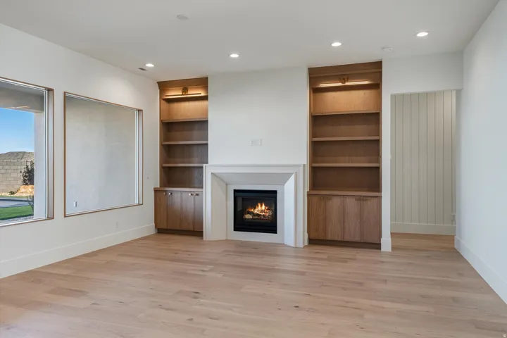 Recessed lighting, wood-finish flooring, central fireplace with stone surround, dual built-in wood cabinetry with integrated shelving