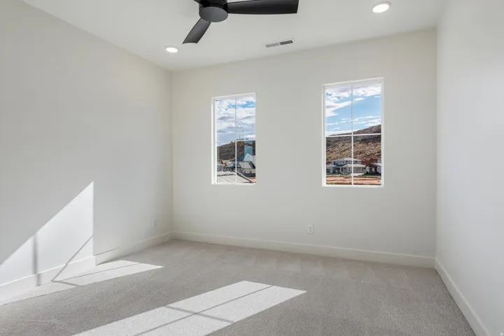 This bedroom has plush carpet flooring, light walls, double-door closet with gold-finish hardware, recessed lighting, and a three windows