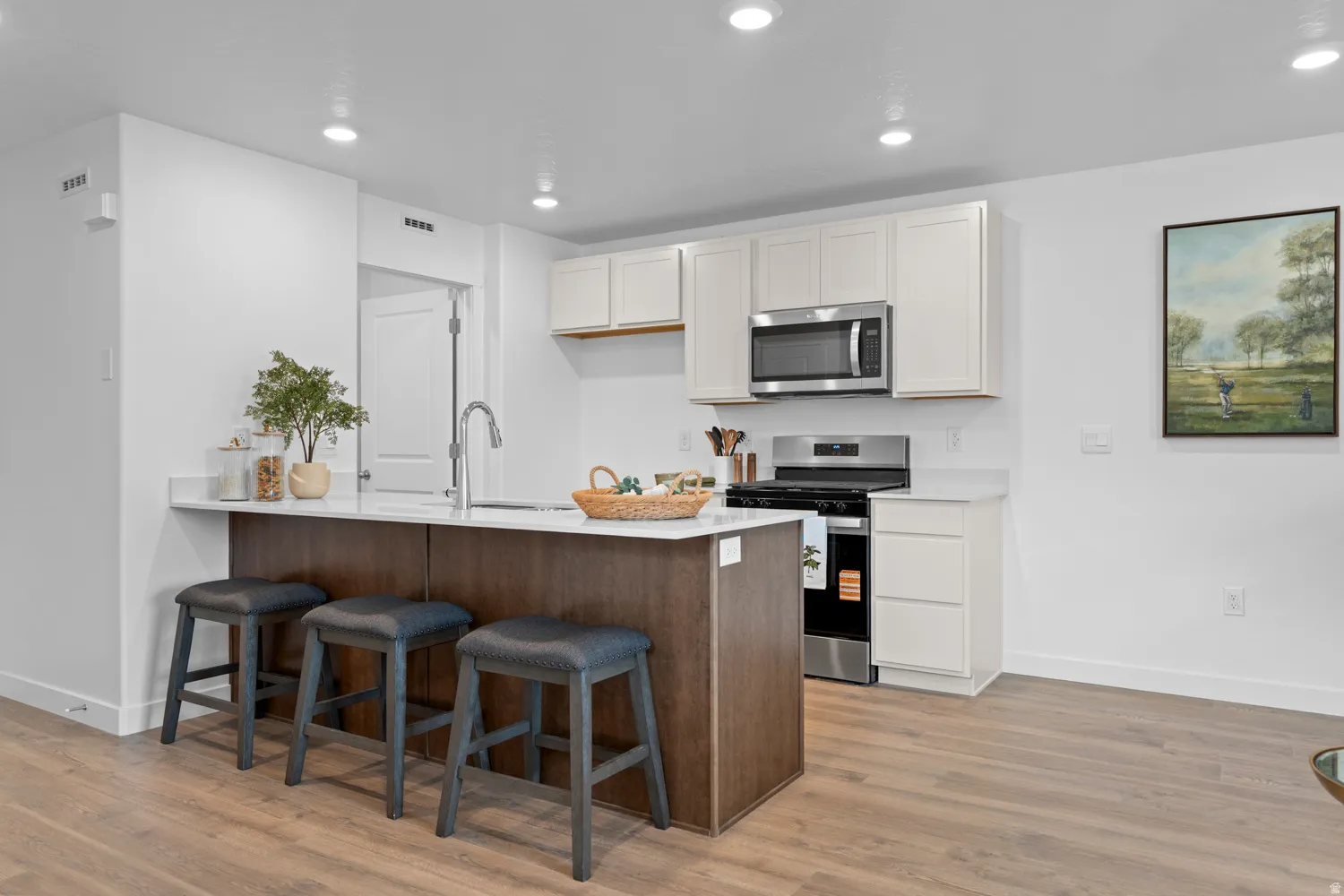Well-appointed kitchen featuring light-toned cabinetry, stainless steel appliances, a center island with countertop seating, and wood-finish flooring