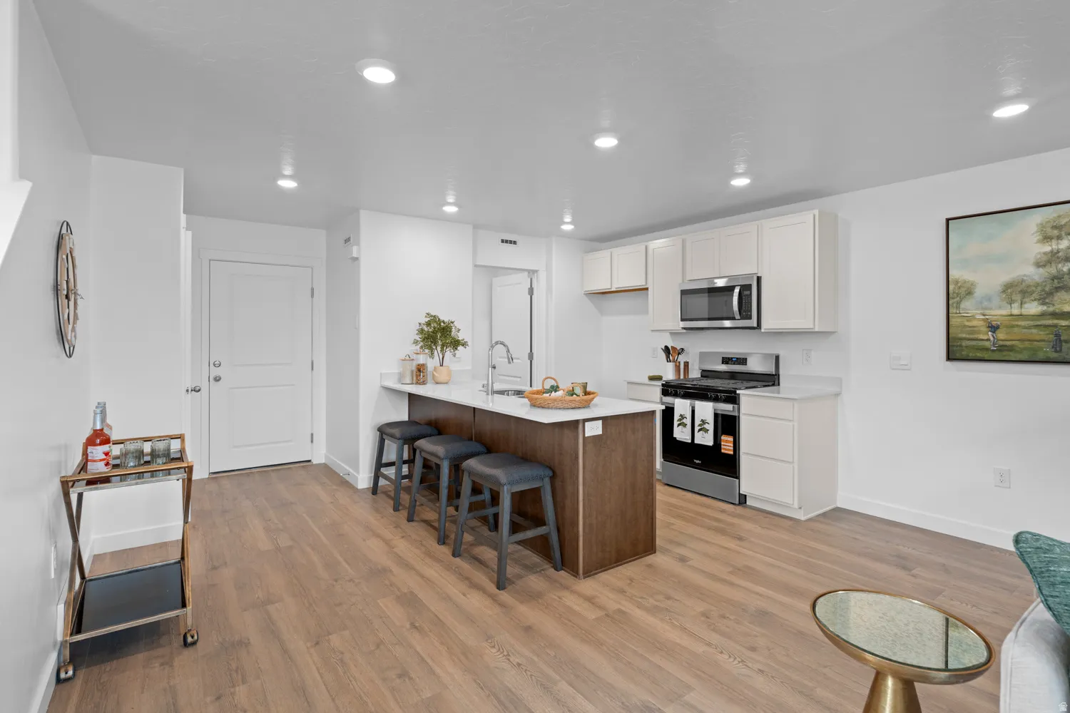 Kitchen featuring an island with a breakfast bar, white cabinetry, a gas range, and a stainless steel microwave