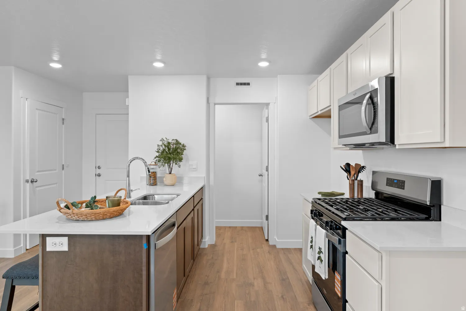 Kitchen featuring wood-finish flooring, recessed lighting, white cabinetry, stainless steel appliances, and an island with an integrated sink