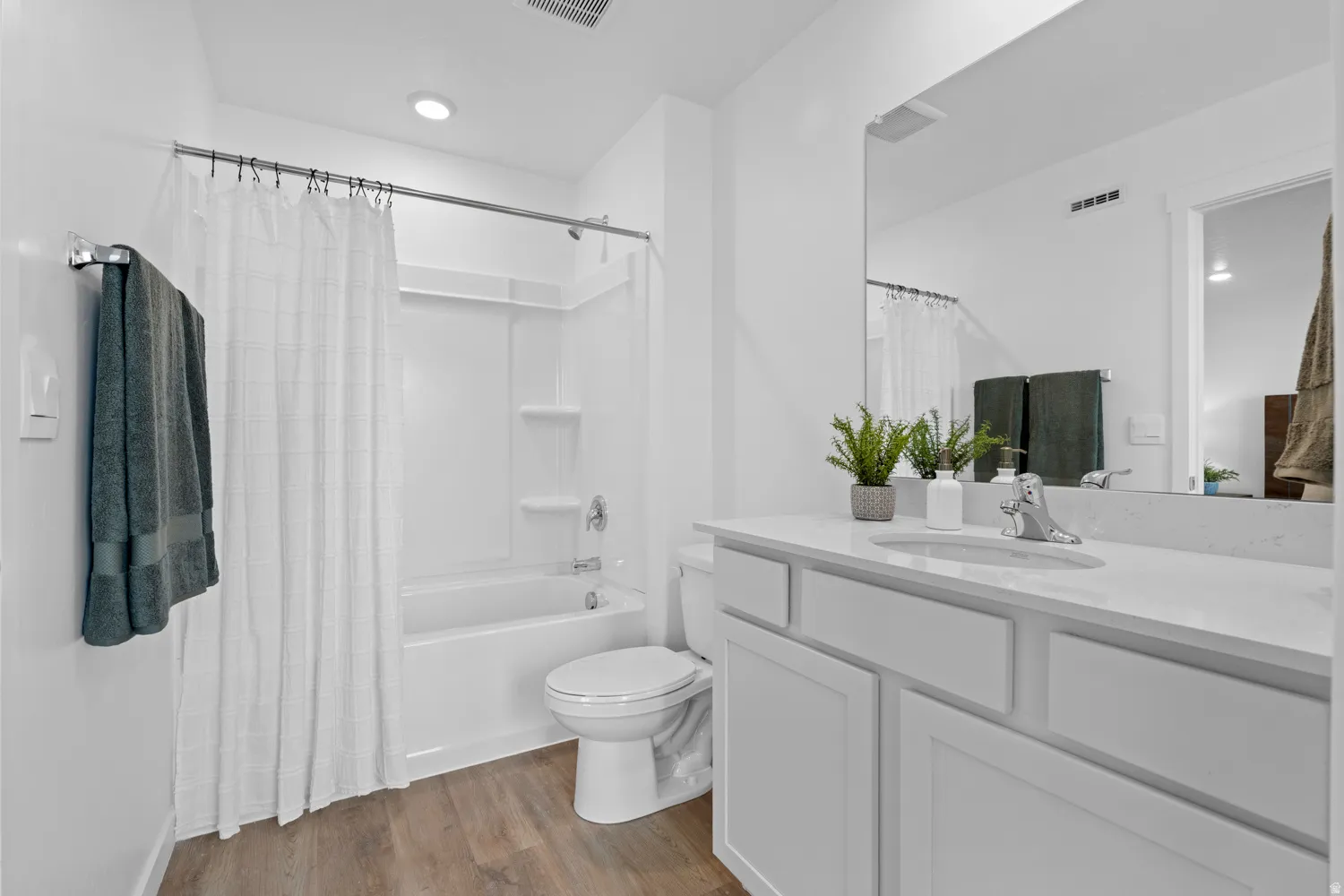 Bathroom featuring a full-size bathtub with shower, wood-finish flooring, a single vanity with stone countertop, and a large wall-mounted mirror