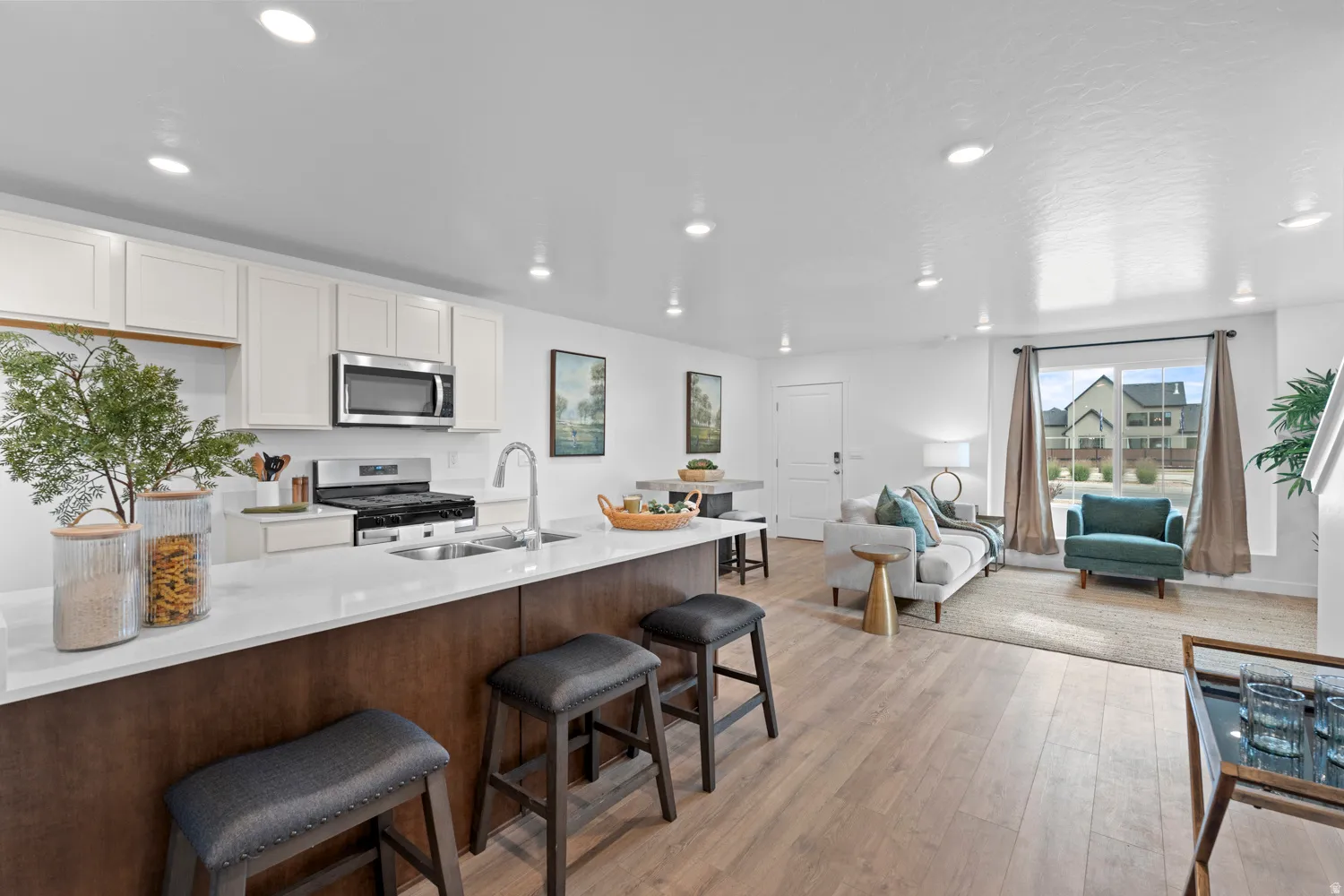 Open-concept living space with wood-finish flooring, white cabinetry, stainless steel appliances, and recessed lighting