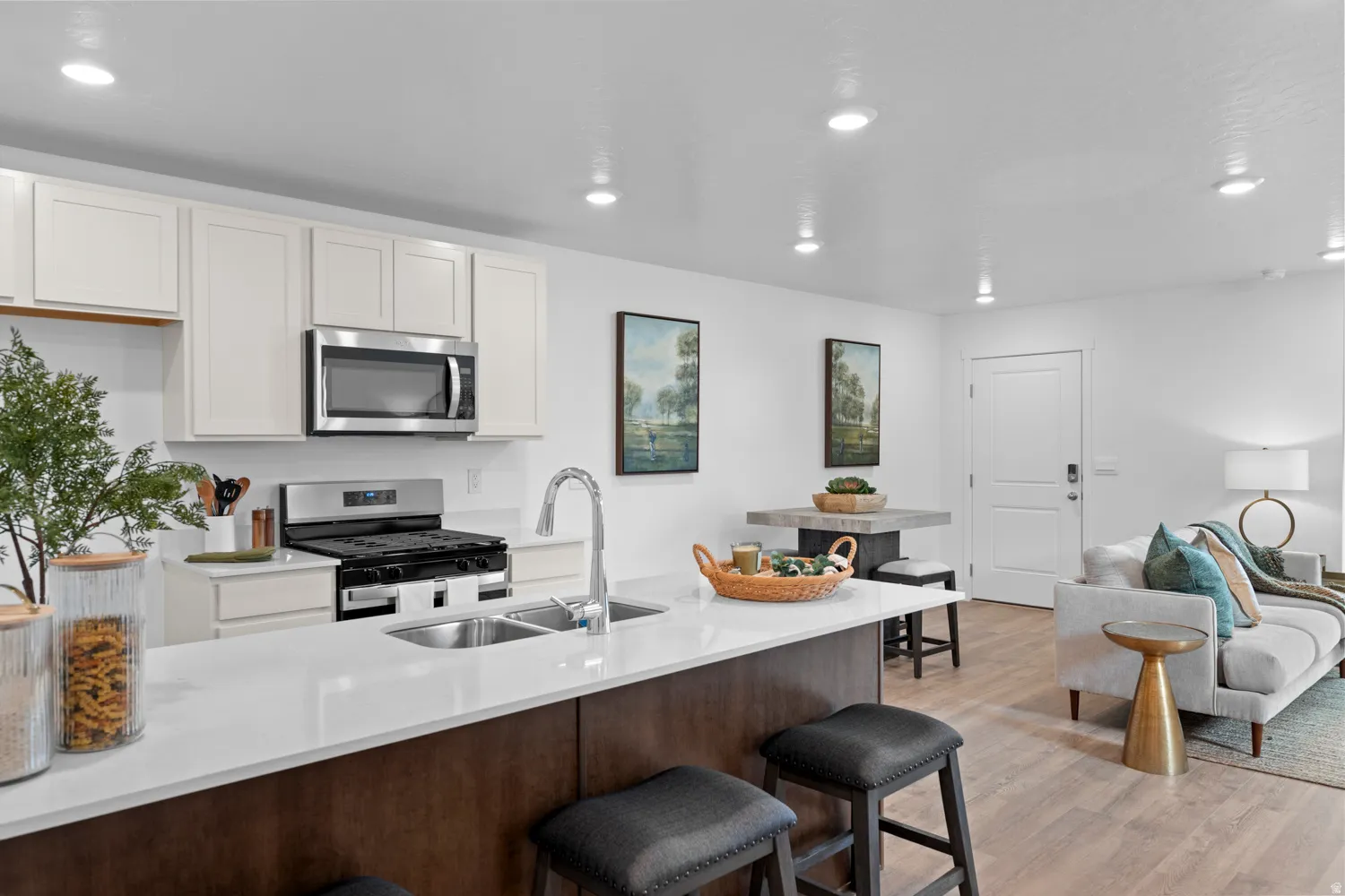 Kitchen featuring white upper cabinetry, a stainless steel gas range, a stainless steel microwave, a dual basin sink, and a white countertop