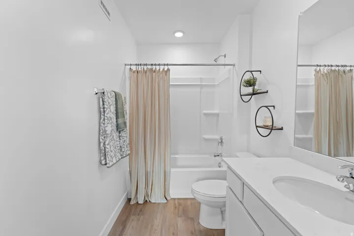 Full bathroom featuring a white vanity with an integrated sink, a full-width mirror, a tub-shower combination, and wood-finish flooring