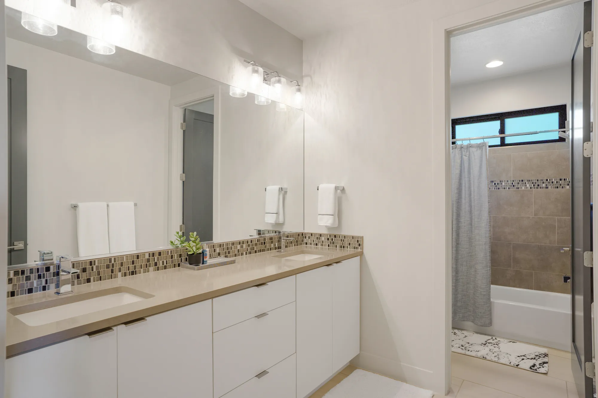 Dual vanity with integrated sinks, contemporary lighting, and a mosaic tile backsplash