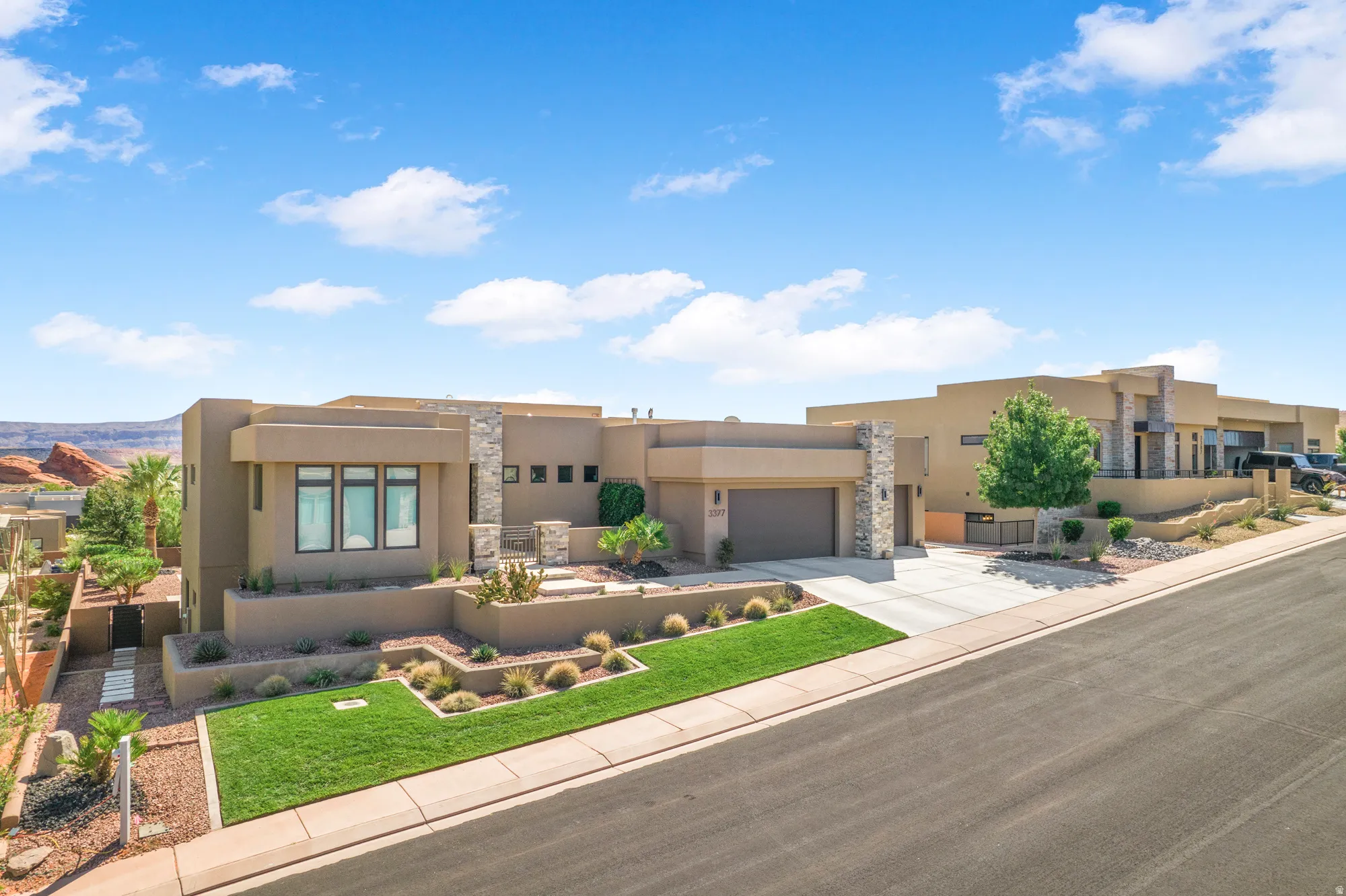 Contemporary stucco exterior with stone accents, integrated garage, terraced landscaping, manicured lawn, and paved driveway