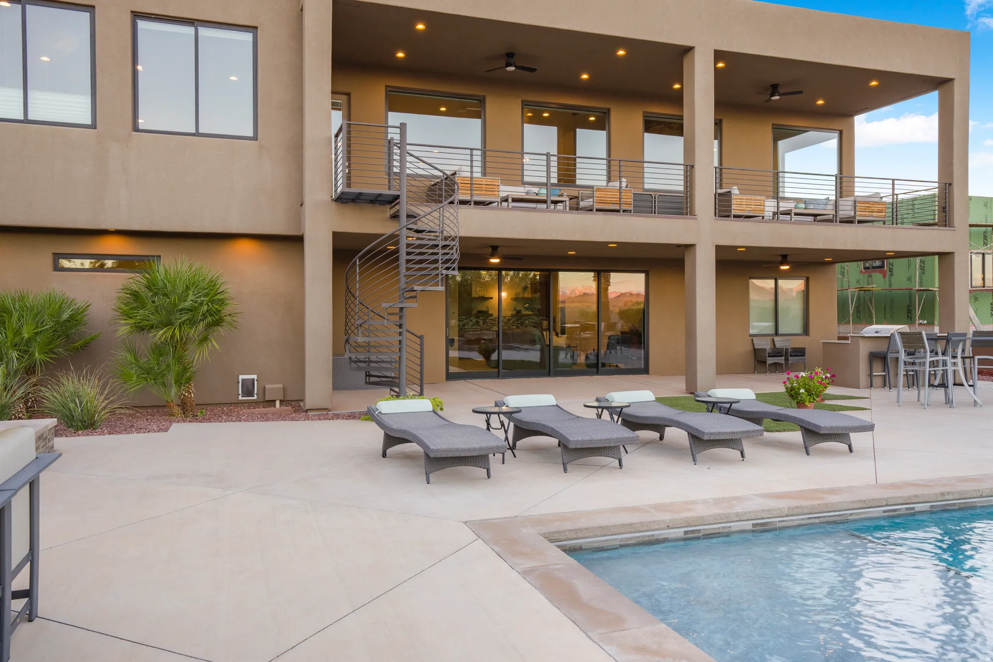 Multi-level exterior with a spiral staircase, multiple balconies with metal railings, an outdoor kitchen area, and a swimming pool