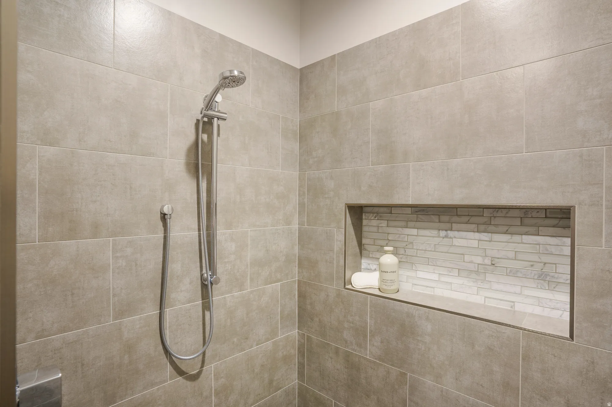 Full-height tiled shower with a handheld showerhead and an integrated niche featuring subway tile