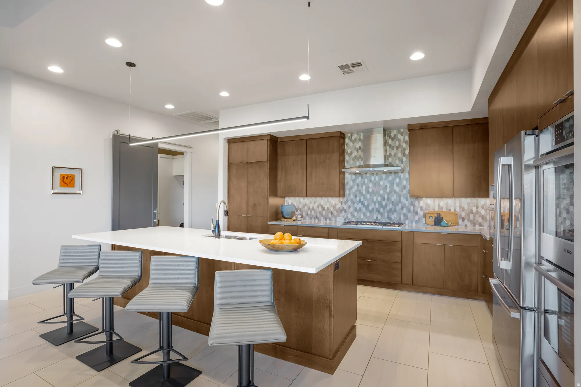 Expansive kitchen island with a white countertop and integrated sink, stainless steel appliances, wood-finish cabinetry, mosaic tile backsplash, and recessed lighting