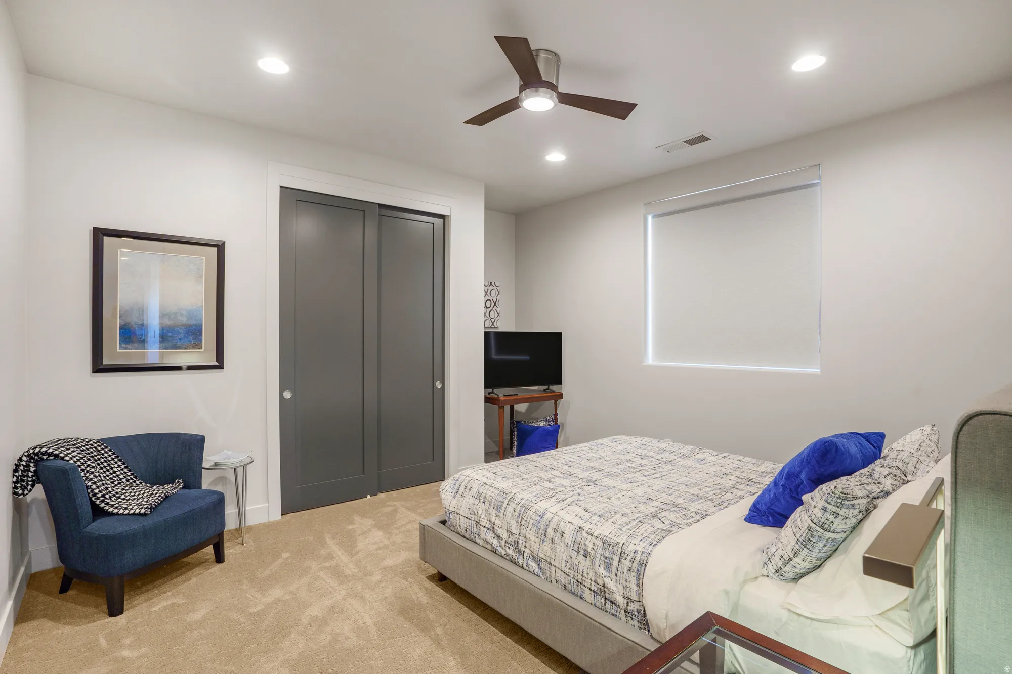 Recessed ceiling lighting, ceiling fan, neutral carpet flooring, window with roller shade, and gray bi-fold closet doors