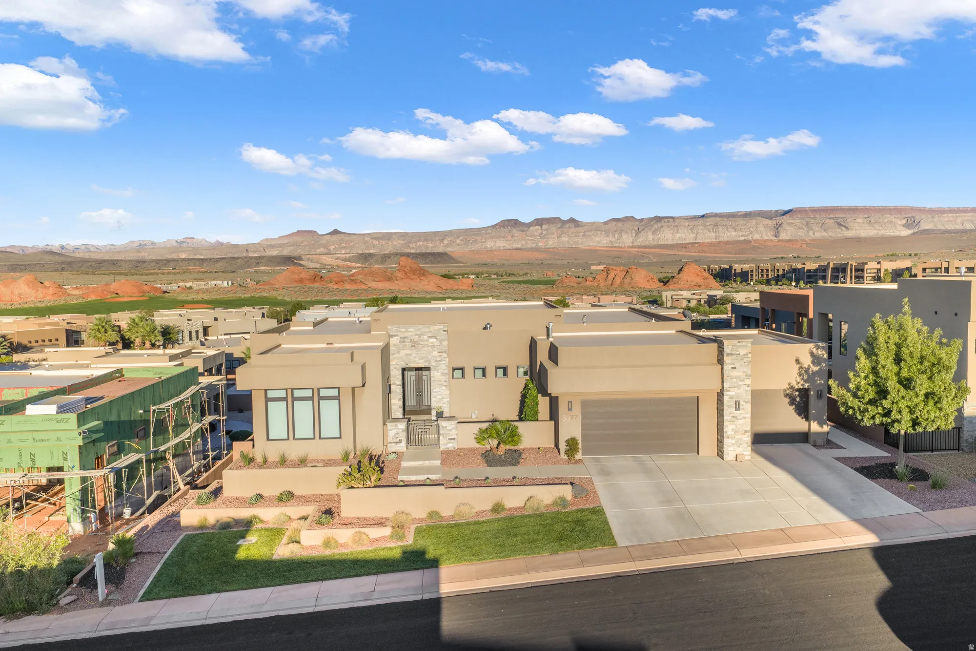 Modern desert architecture with flat rooflines, stone facade accents, a two-car garage, manicured landscaping, and a mountain backdrop