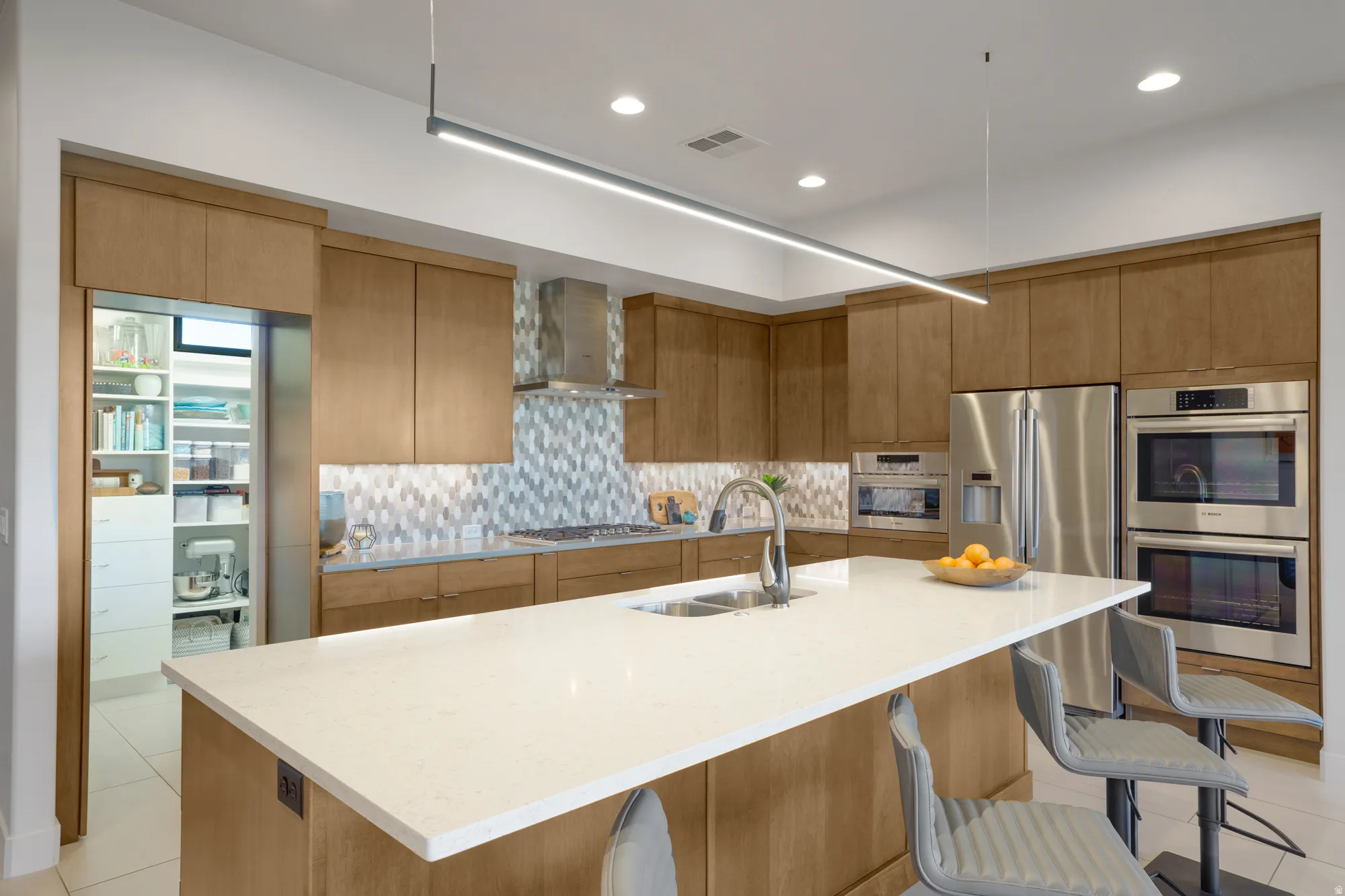 Kitchen featuring wood cabinetry, stainless steel appliances, a center island with a sink, and a walk-in pantry with shelving