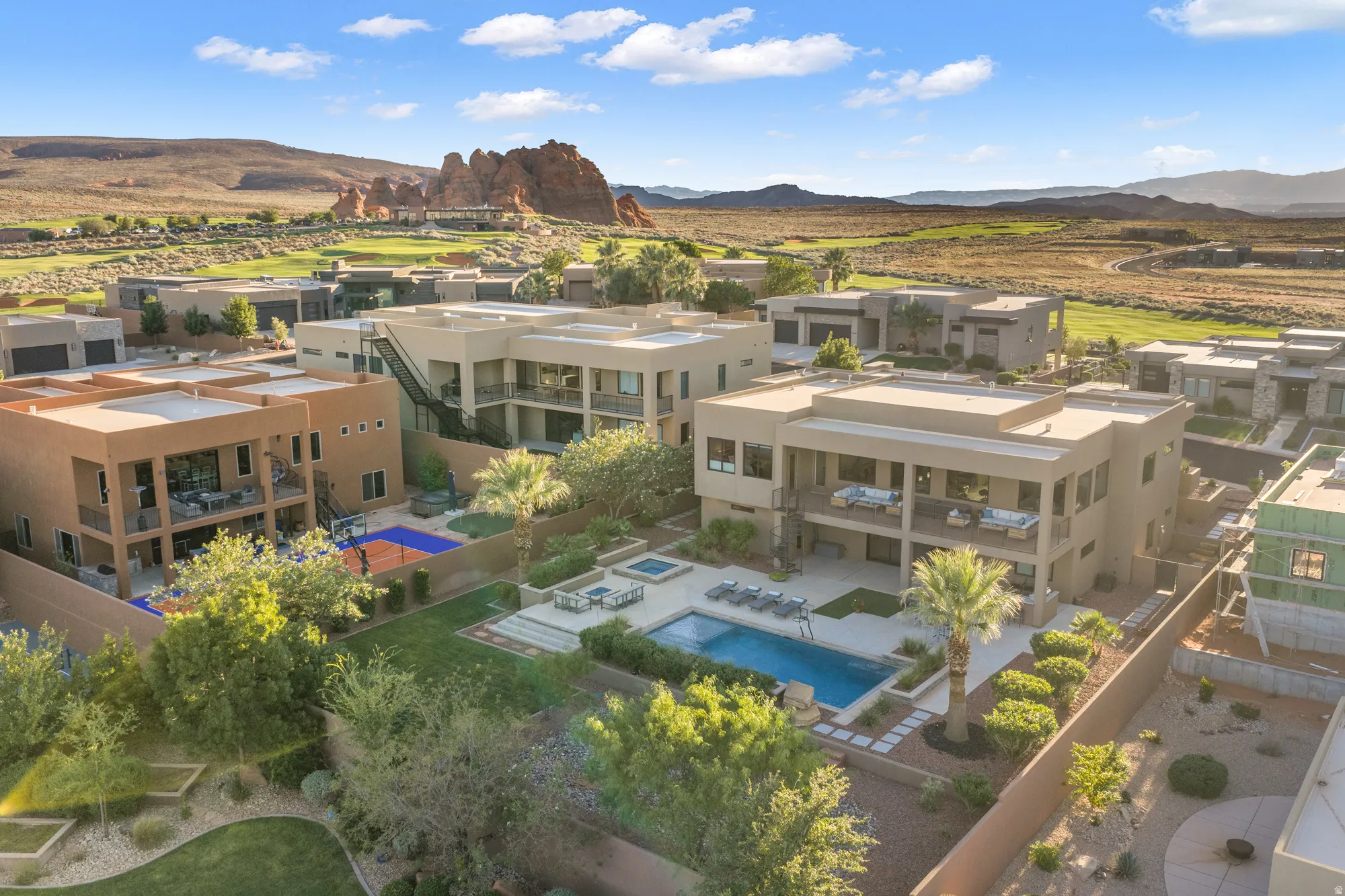 Modern residential architecture with multiple balconies, a private swimming pool, and a sports court, all surrounded by arid landscaping and distant red rock formations