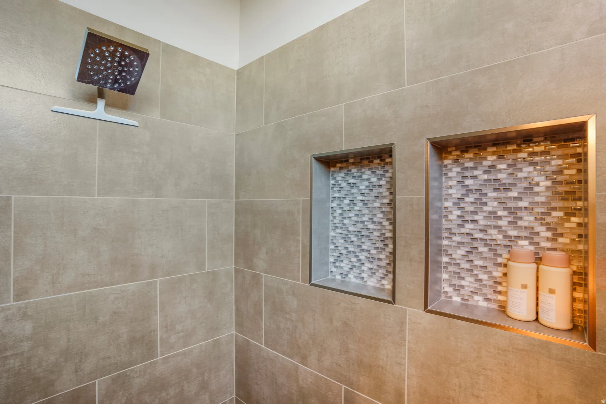 Tiled shower with a square rain showerhead, two recessed niches, and mosaic tile accents