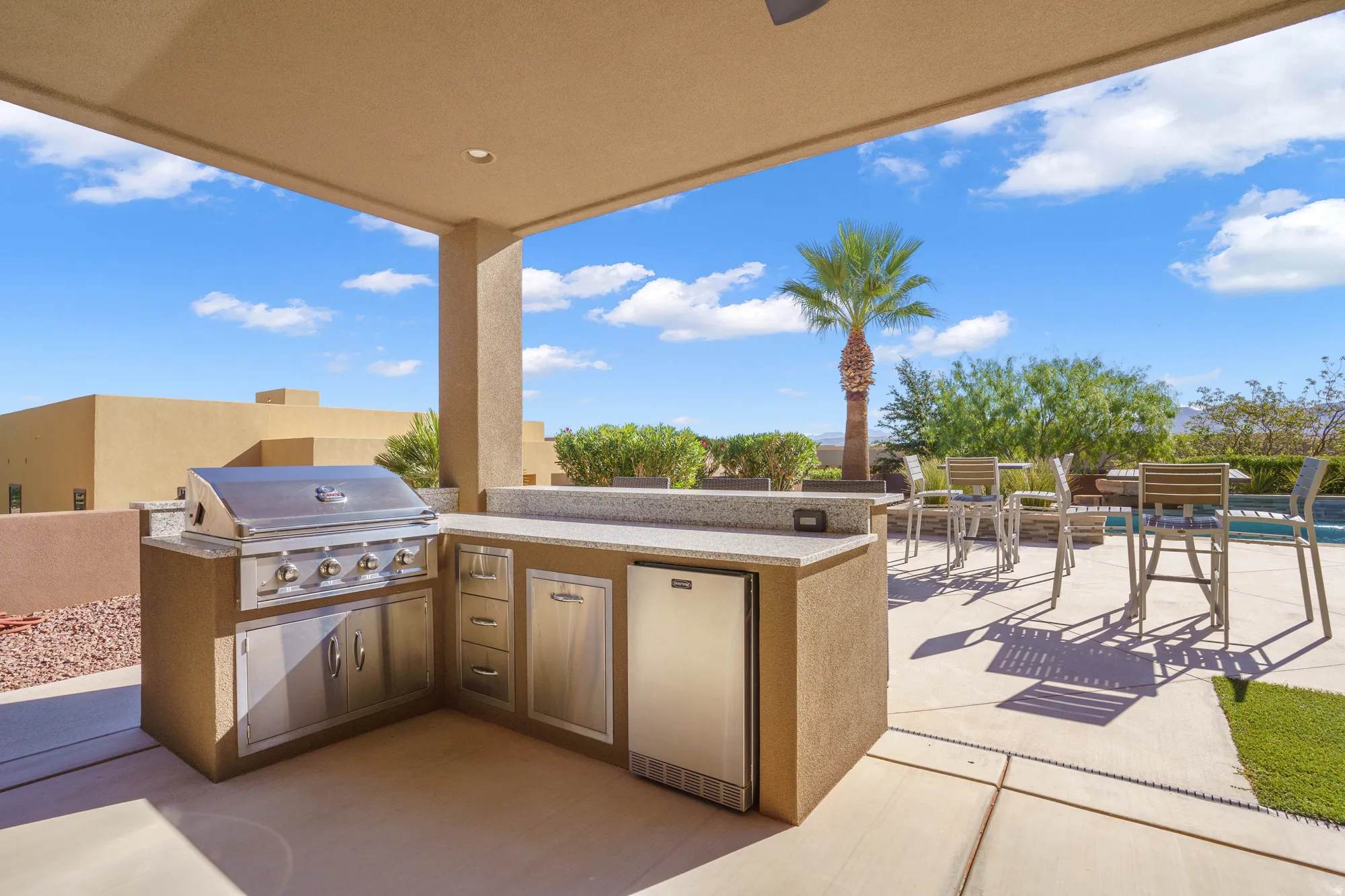 Covered outdoor kitchen featuring a built-in grill, integrated beverage cooler, and stone-finish countertops