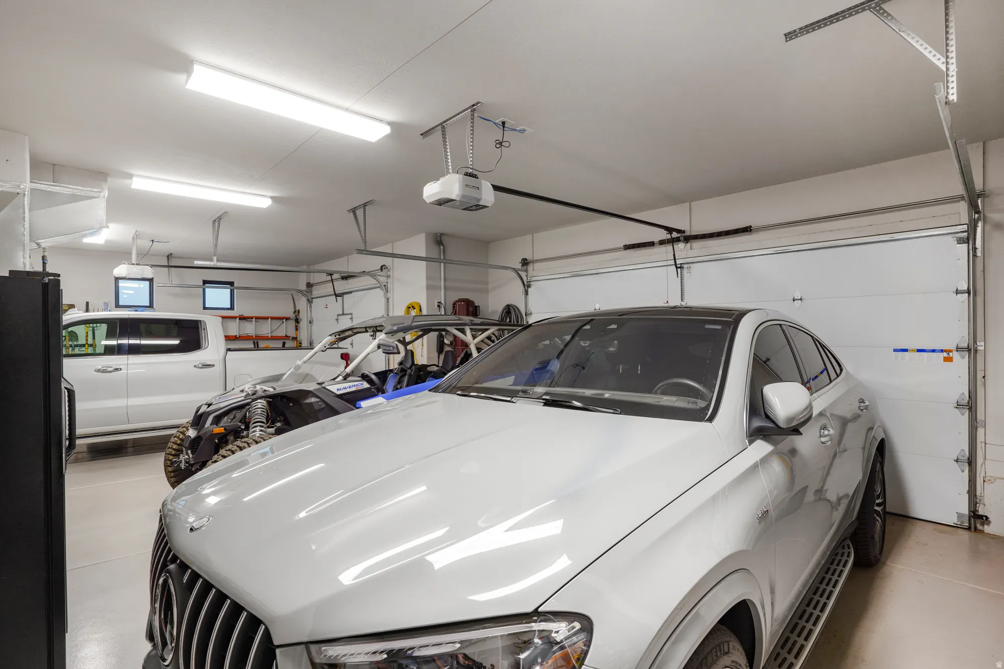Spacious garage featuring multiple garage doors, overhead lighting, and built-in shelving