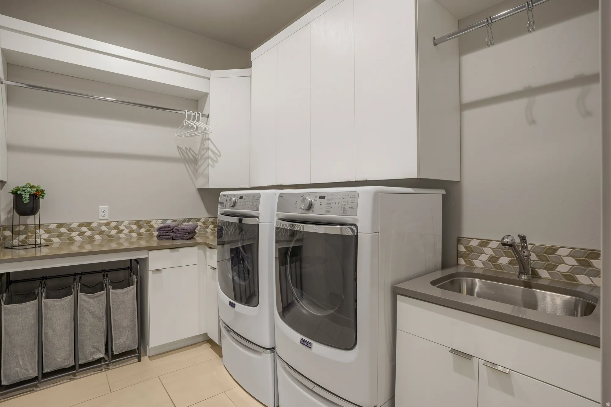 Laundry room featuring a utility sink, upper and lower cabinetry, a hanging rod, and tile flooring