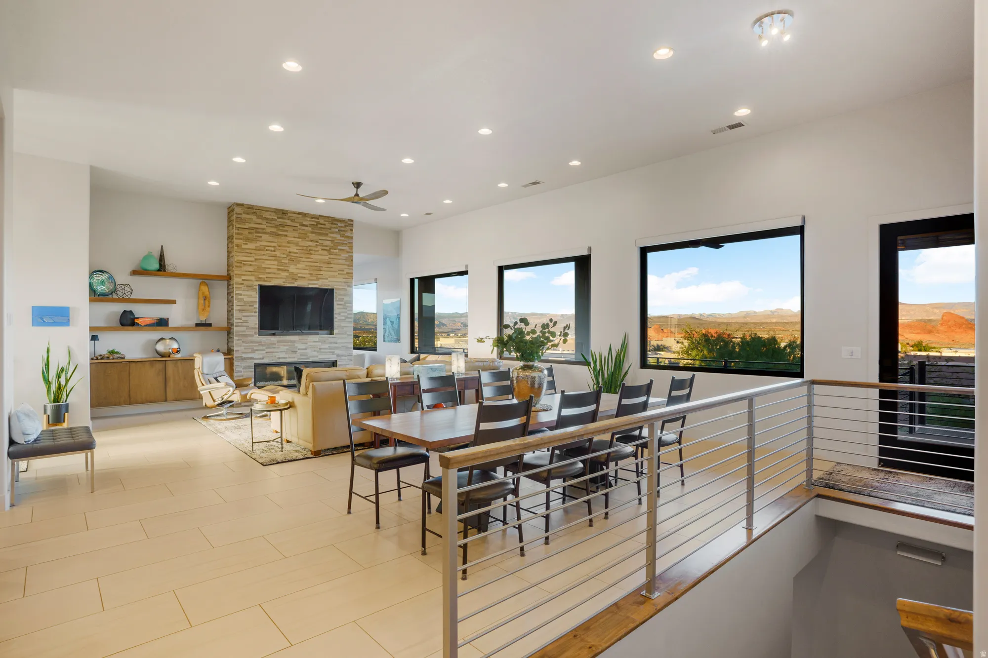 Open-concept living area with a stone-clad fireplace, integrated shelving, and large windows