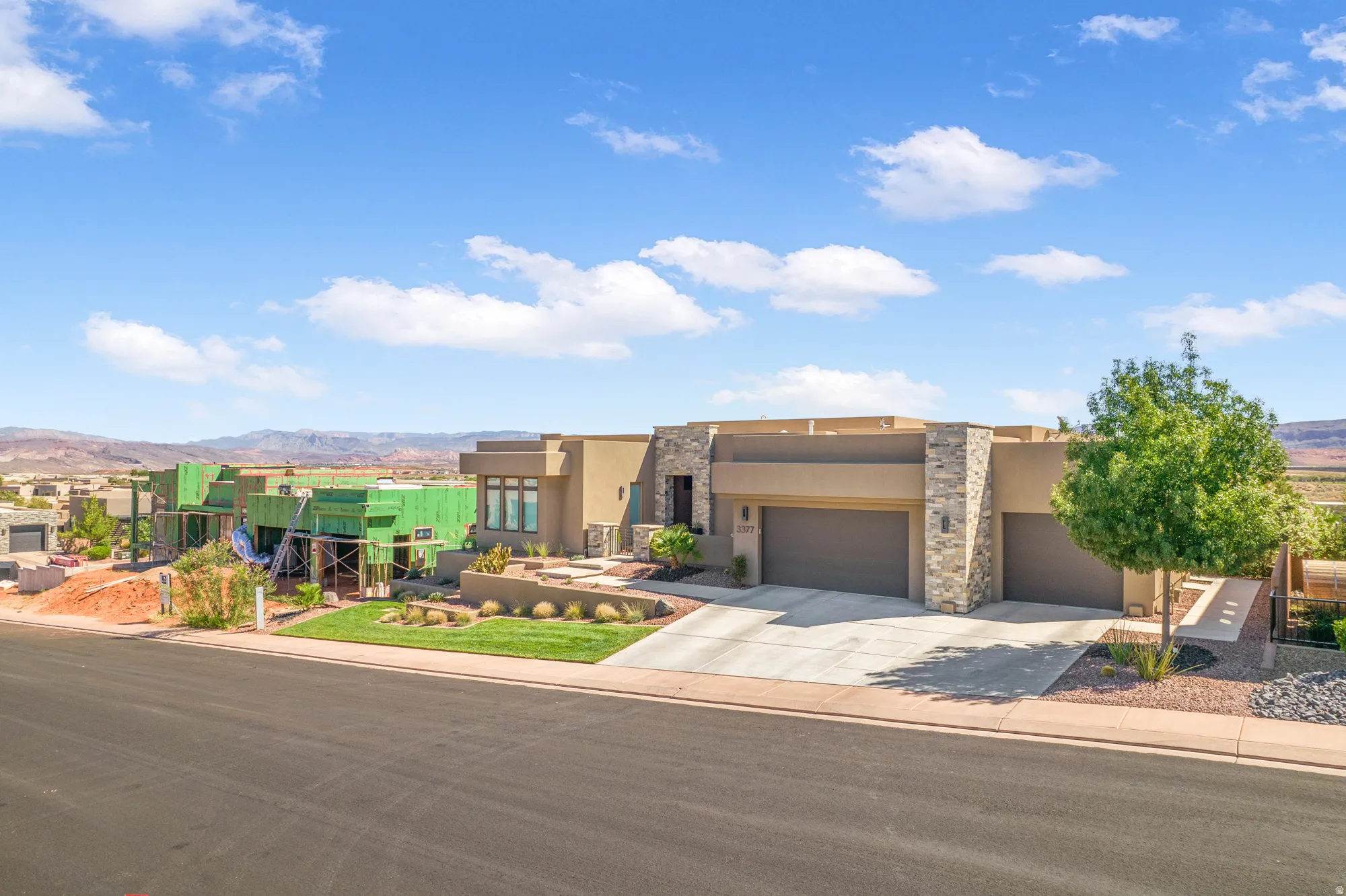 Modern stucco exterior with stone accents, a dual-car garage, concrete driveway, and landscaped front yard
