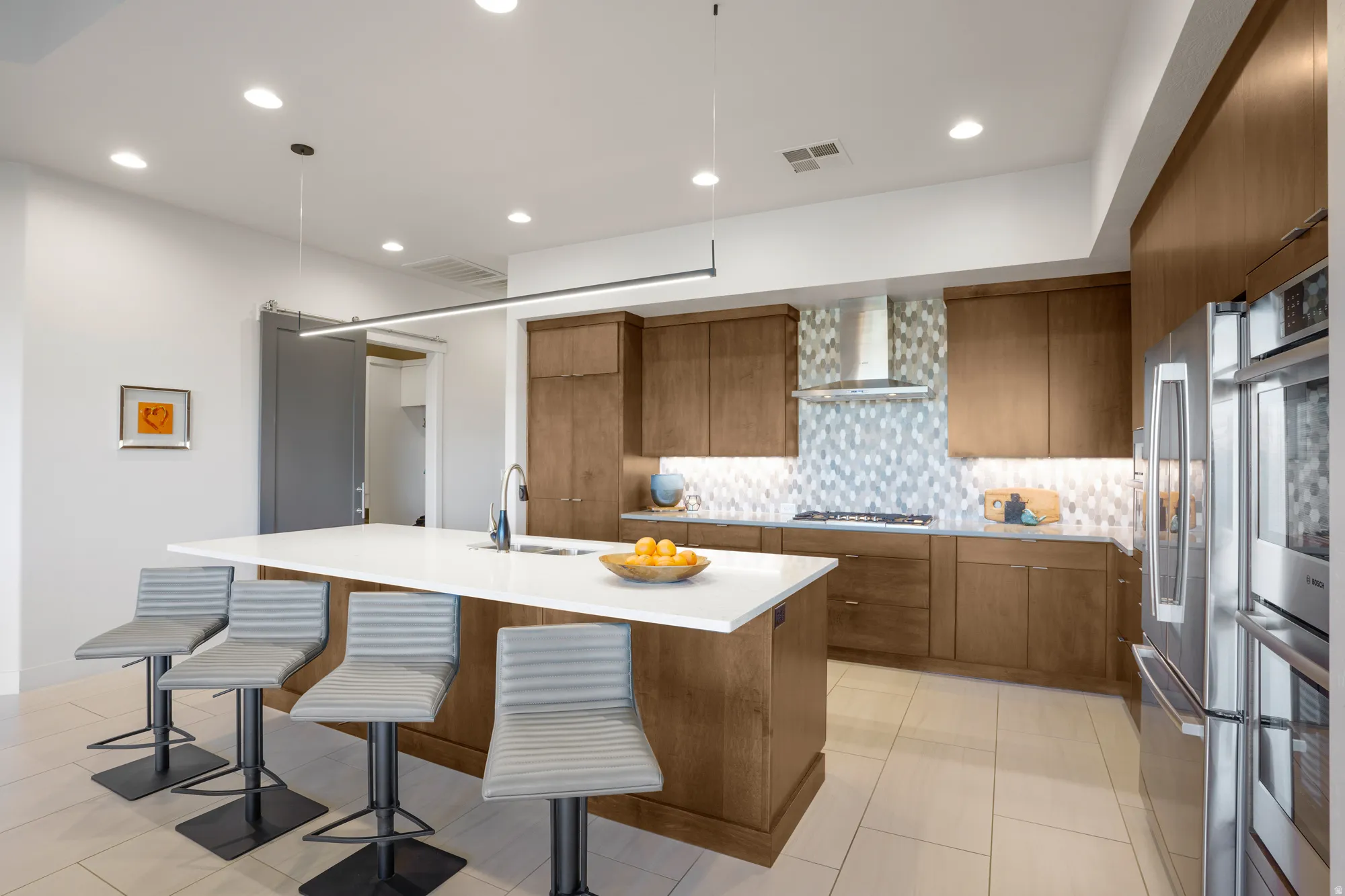 Kitchen featuring a large island with sink, wood cabinetry, stainless steel appliances, and a unique tiled backsplash