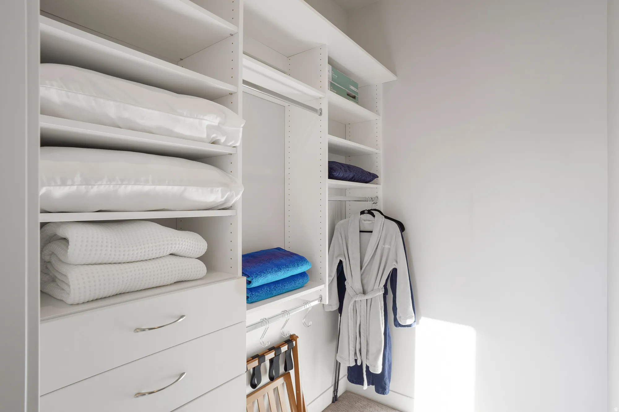 Custom closet organization system featuring white shelving, built-in drawers with chrome hardware, and hanging rods