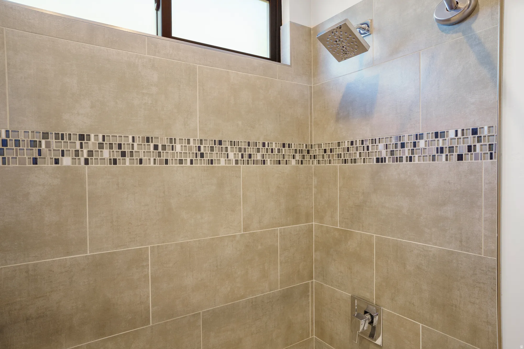 Shower with neutral-toned rectangular tile, mosaic accent band, and rainfall showerhead