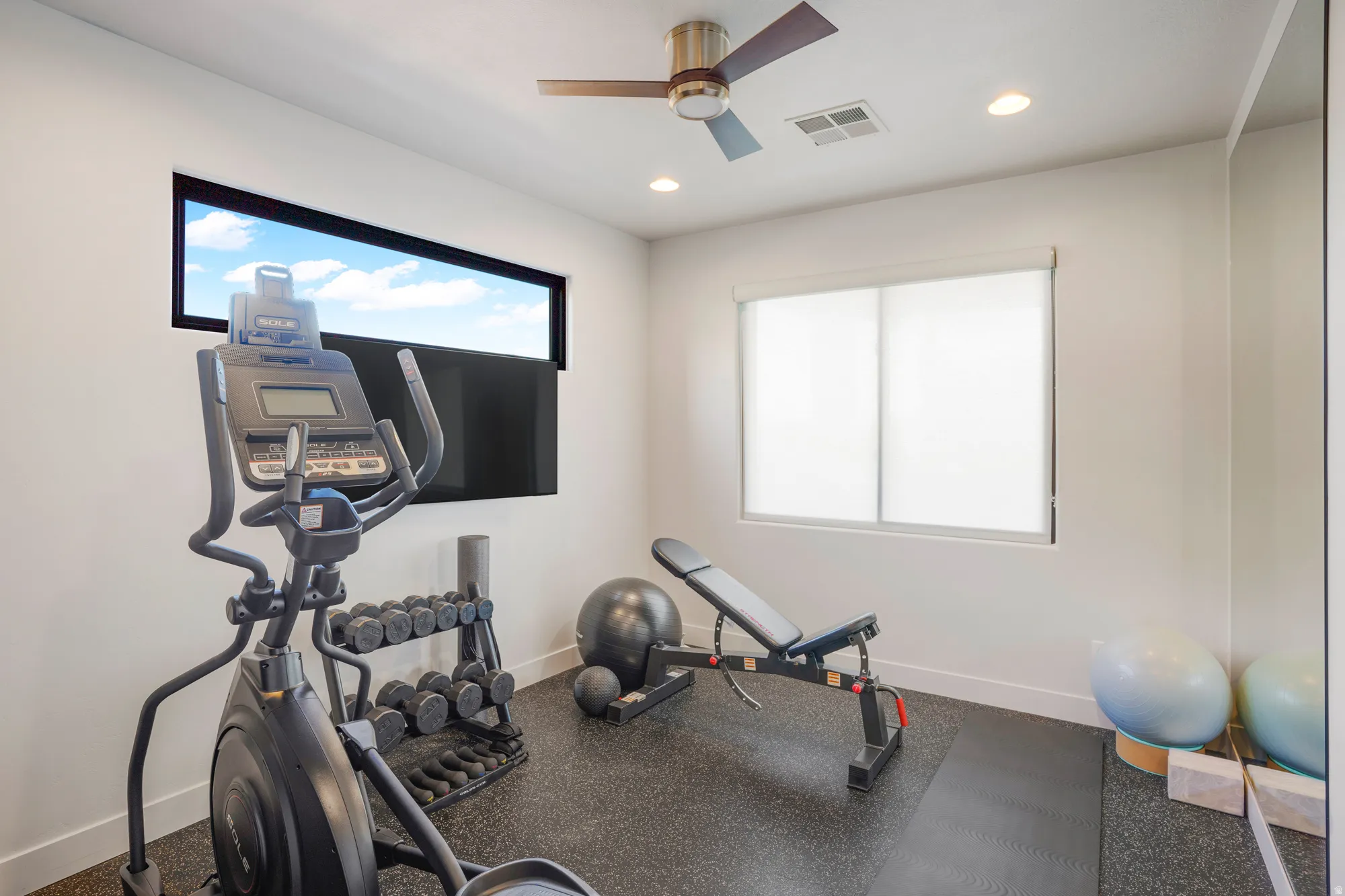 Recessed lighting, ceiling fan, large window with roller shades, high horizontal accent window, and dark flooring