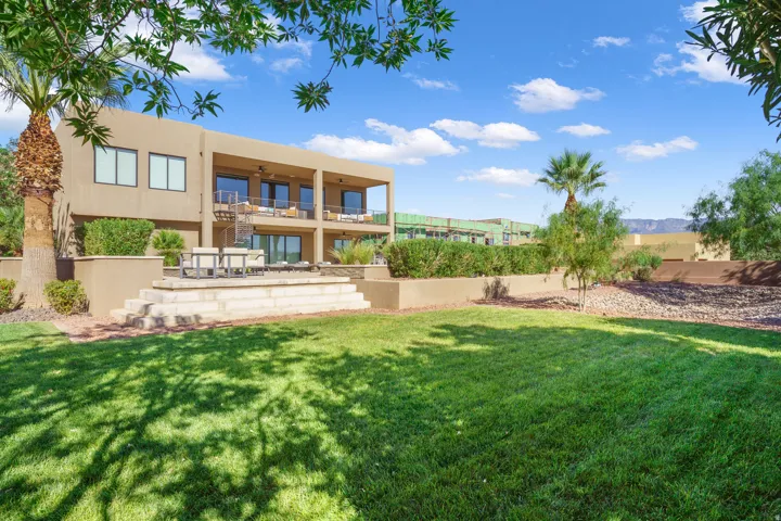 Expansive rear lawn, multi-level terrace, upper-level balcony, lower-level patio, and mature landscaping