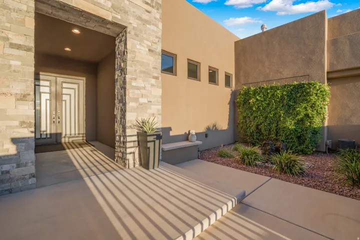 Stucco exterior featuring stacked stone accents, a double entry door with geometric detailing, recessed lighting, and a landscaped courtyard with decorative shrubs