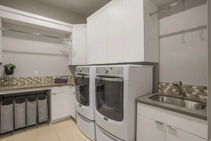 Laundry room featuring a utility sink, upper and lower cabinetry, a hanging rod, and tile flooring