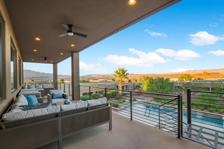Expansive outdoor balcony with recessed lighting, ceiling fans, and a metal railing system overlooking a swimming pool and distant mountains