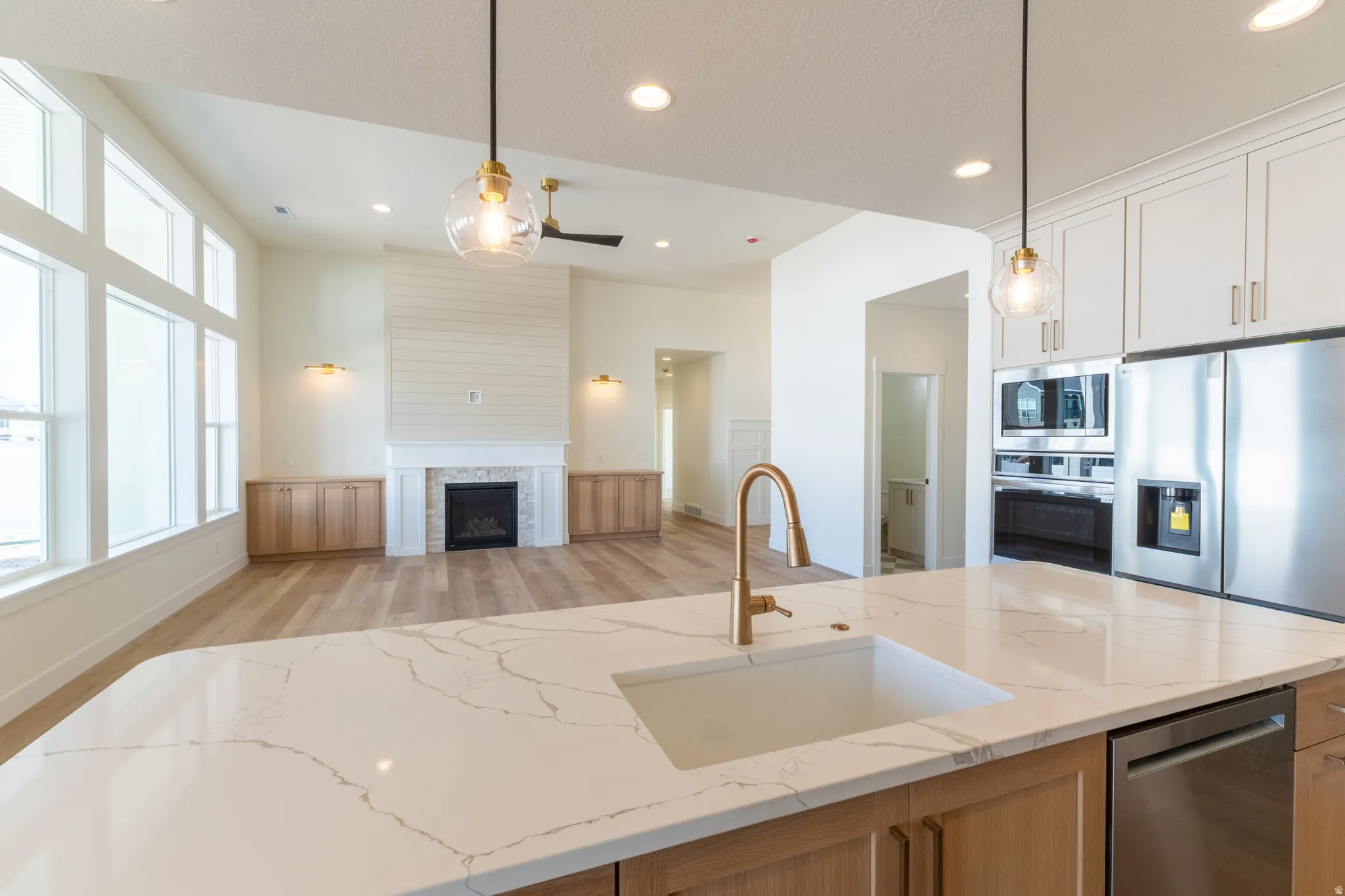 Large kitchen island with a white sink and gold-finish faucet, stainless steel appliances, and white cabinetry