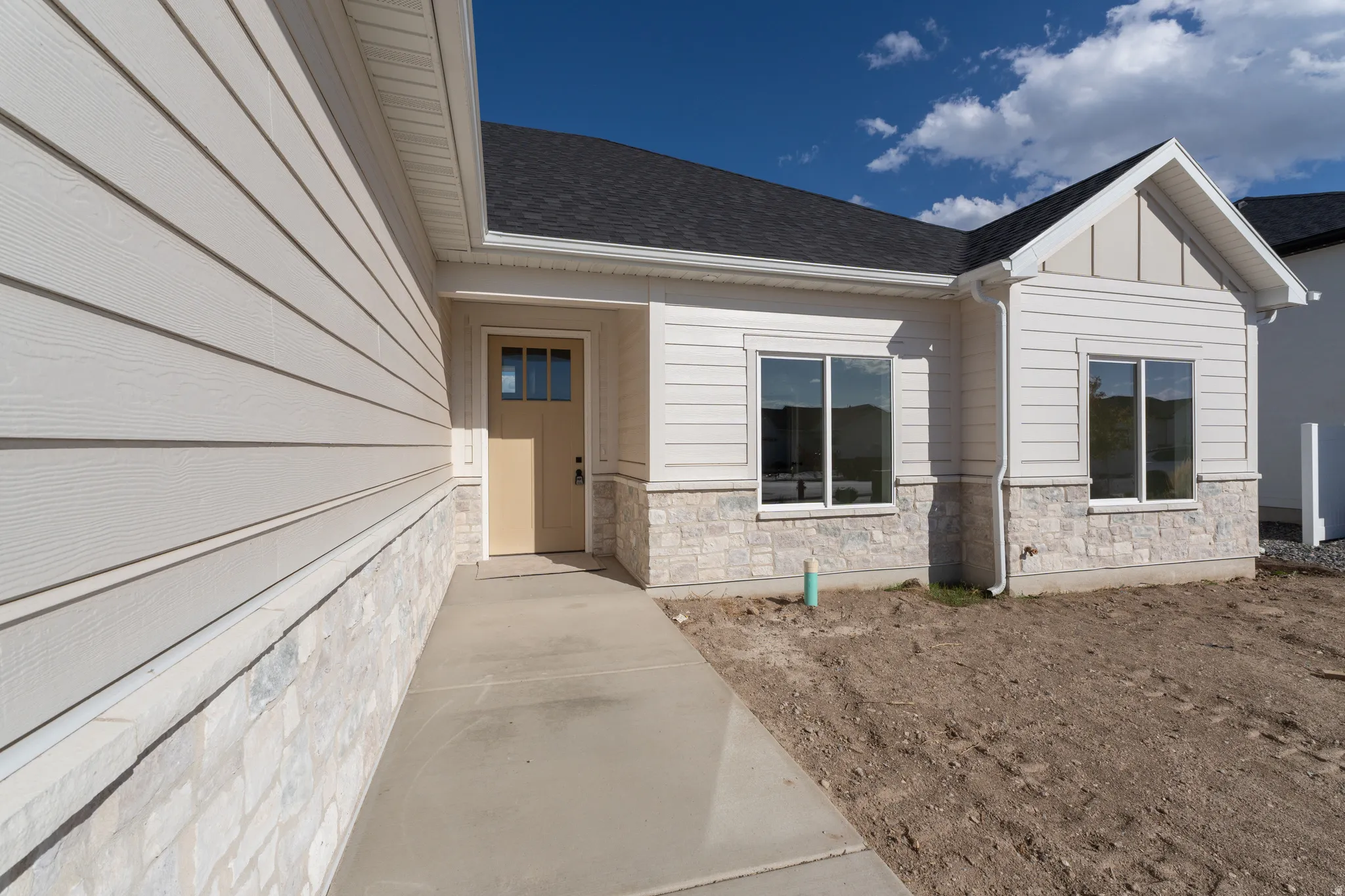 White siding exterior with stone accent, dark shingle roof, and a beige entry door