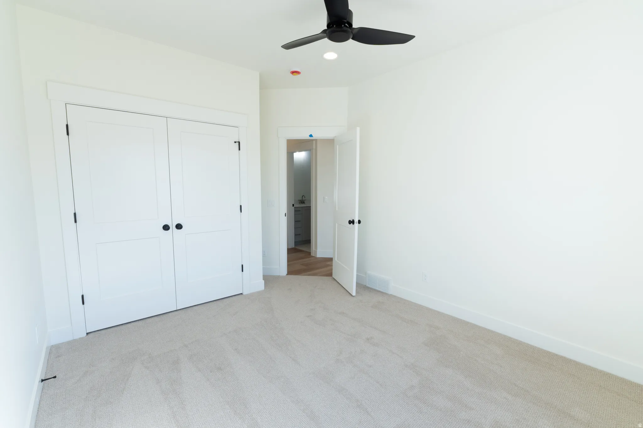 Neutral tone wall finishes, soft carpet flooring, black ceiling fan, recessed lighting, and a double-door closet
