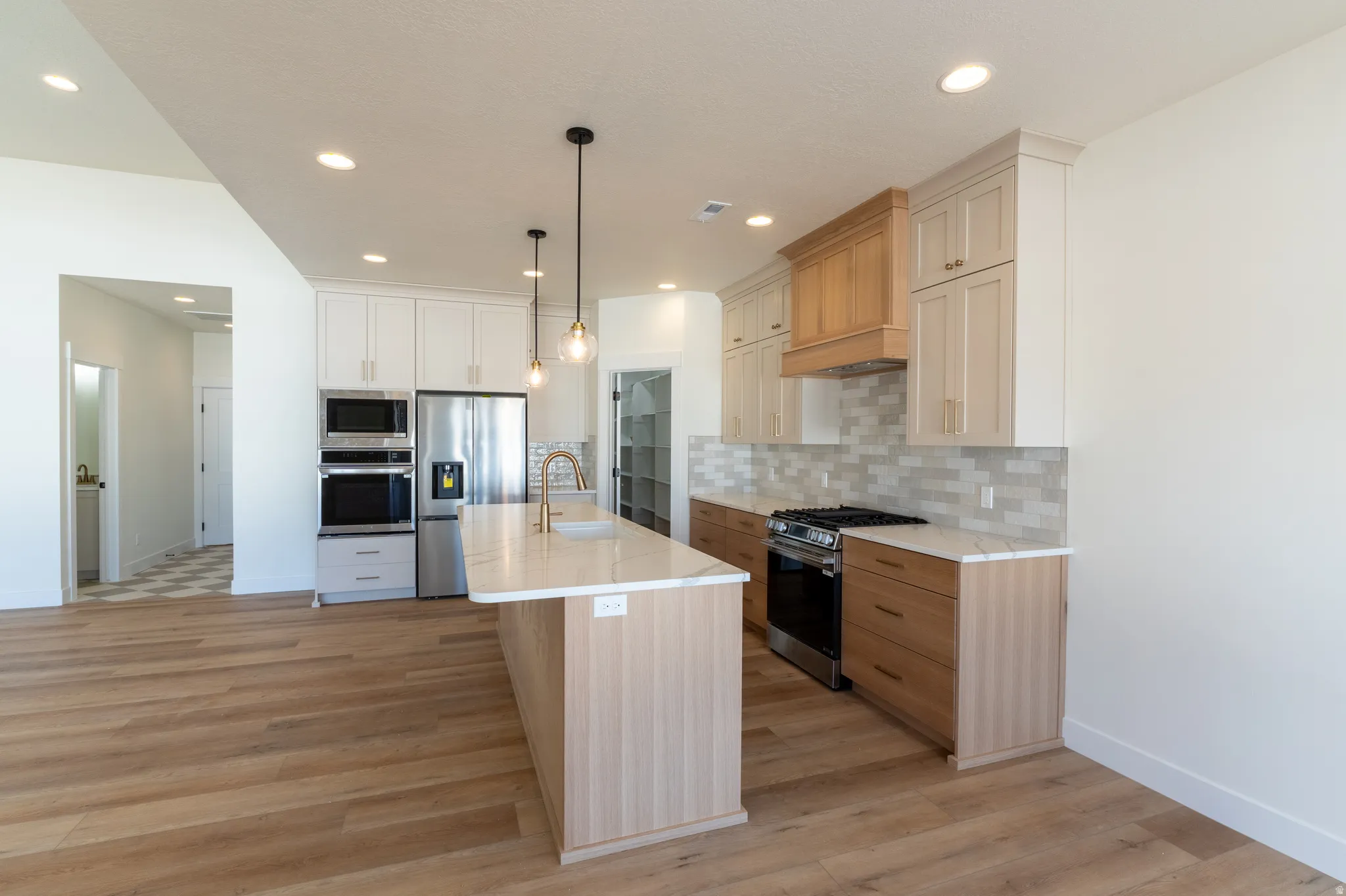 Open-concept kitchen featuring an island with a sink, stainless steel appliances, light wood-finish flooring, and white and natural wood cabinetry