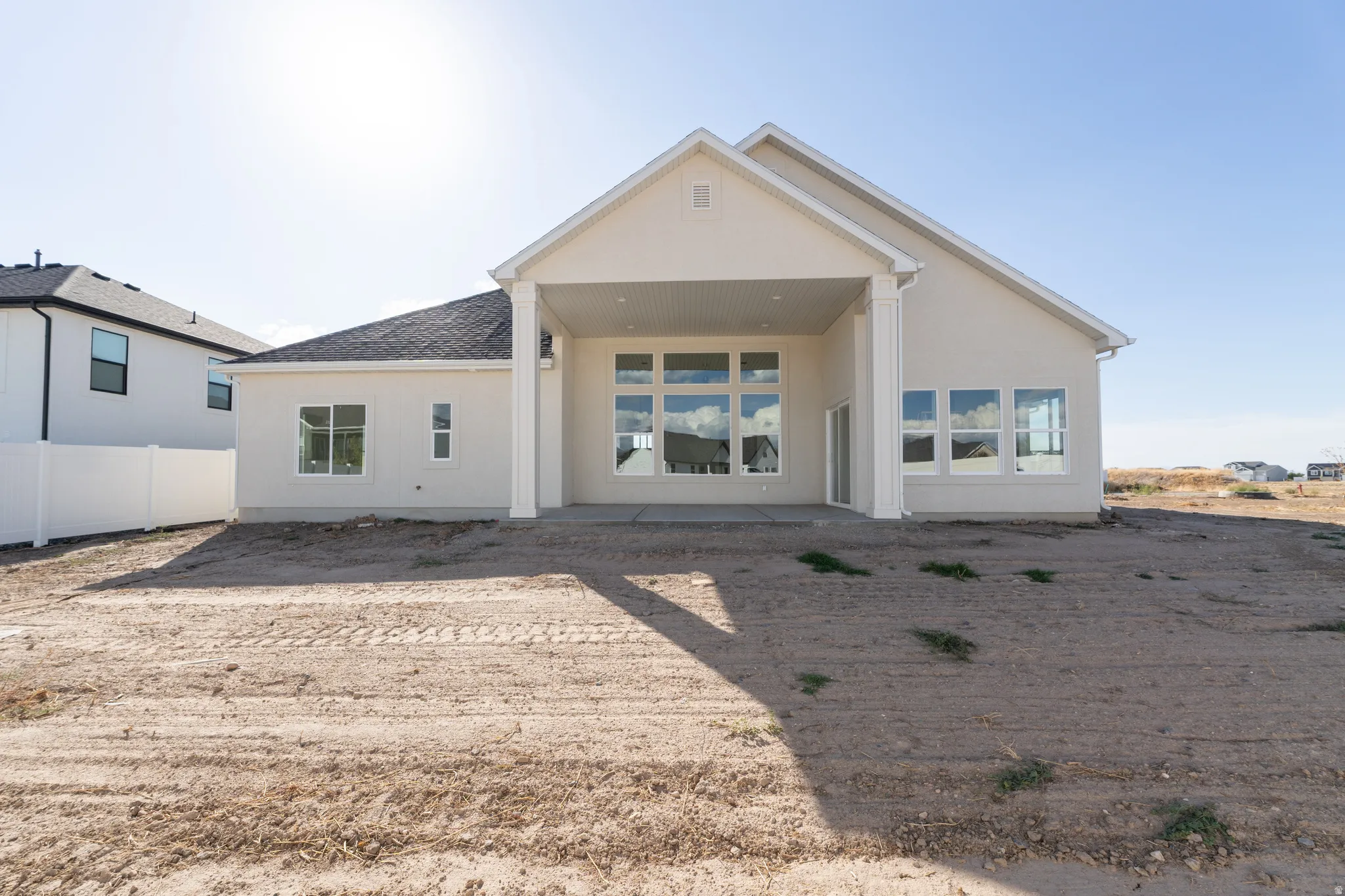 Rear elevation featuring an expansive covered patio, multiple large windows, and a white privacy fence