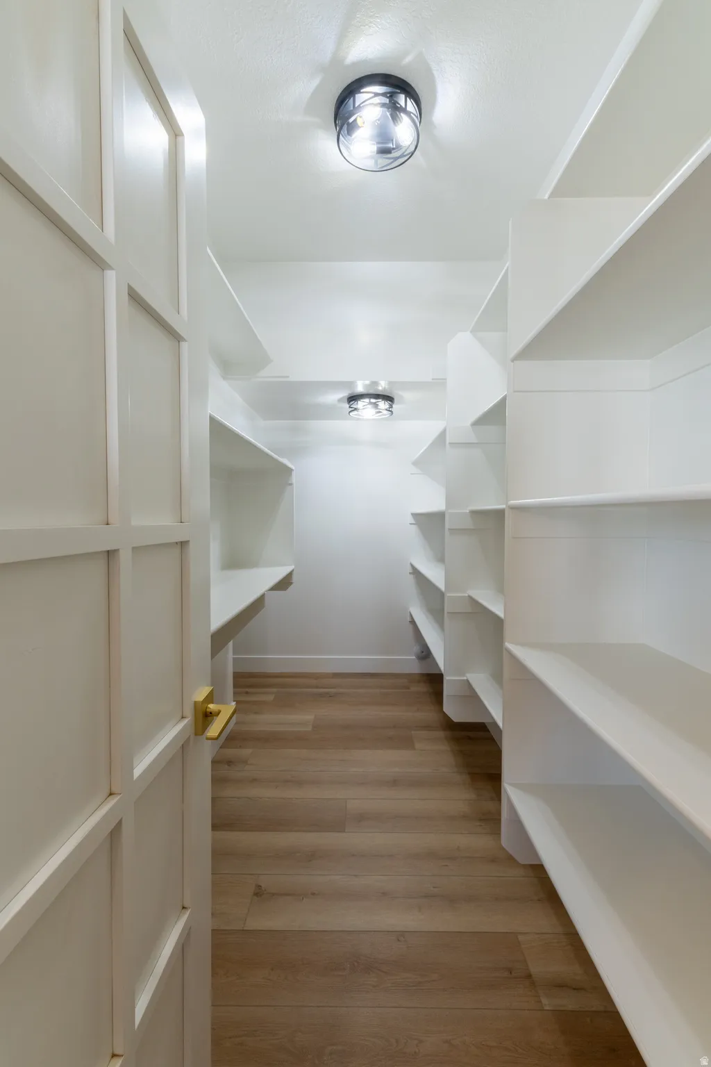 Walk-in pantry featuring extensive built-in shelving, wood-finish flooring, and recessed ceiling lighting