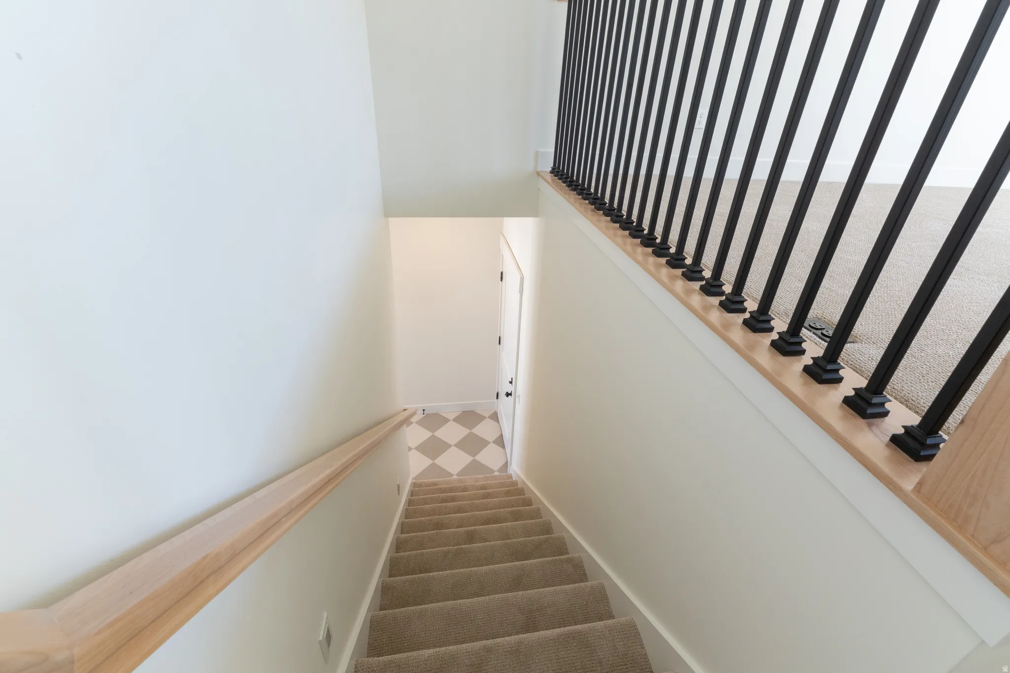 Carpeted staircase with light wood-finish handrails and black metal balusters. Upstairs to open loft.
