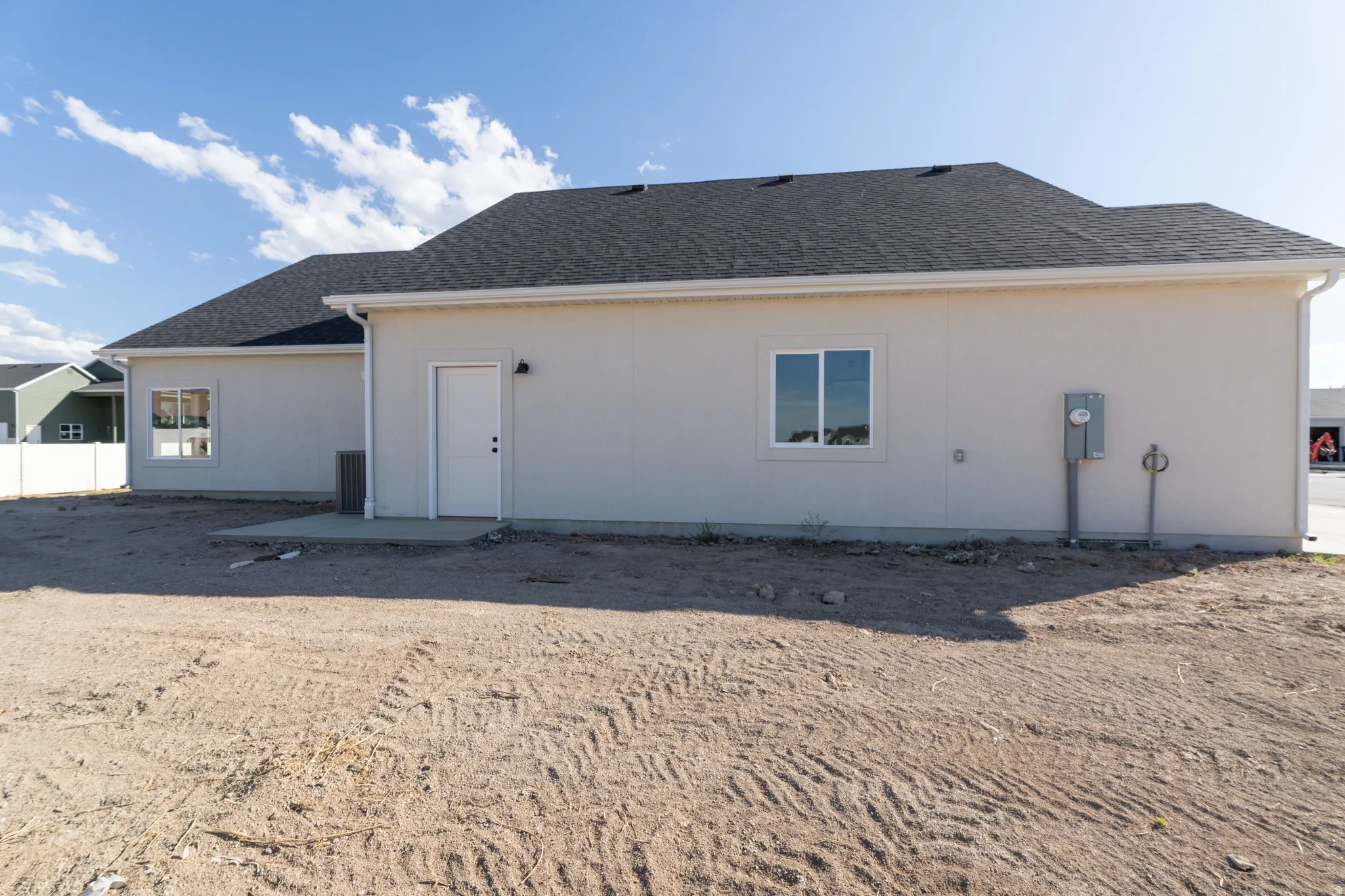 Exterior featuring a dark shingle roof, light-colored stucco siding, white window trim, a side entry door, and a concrete patio