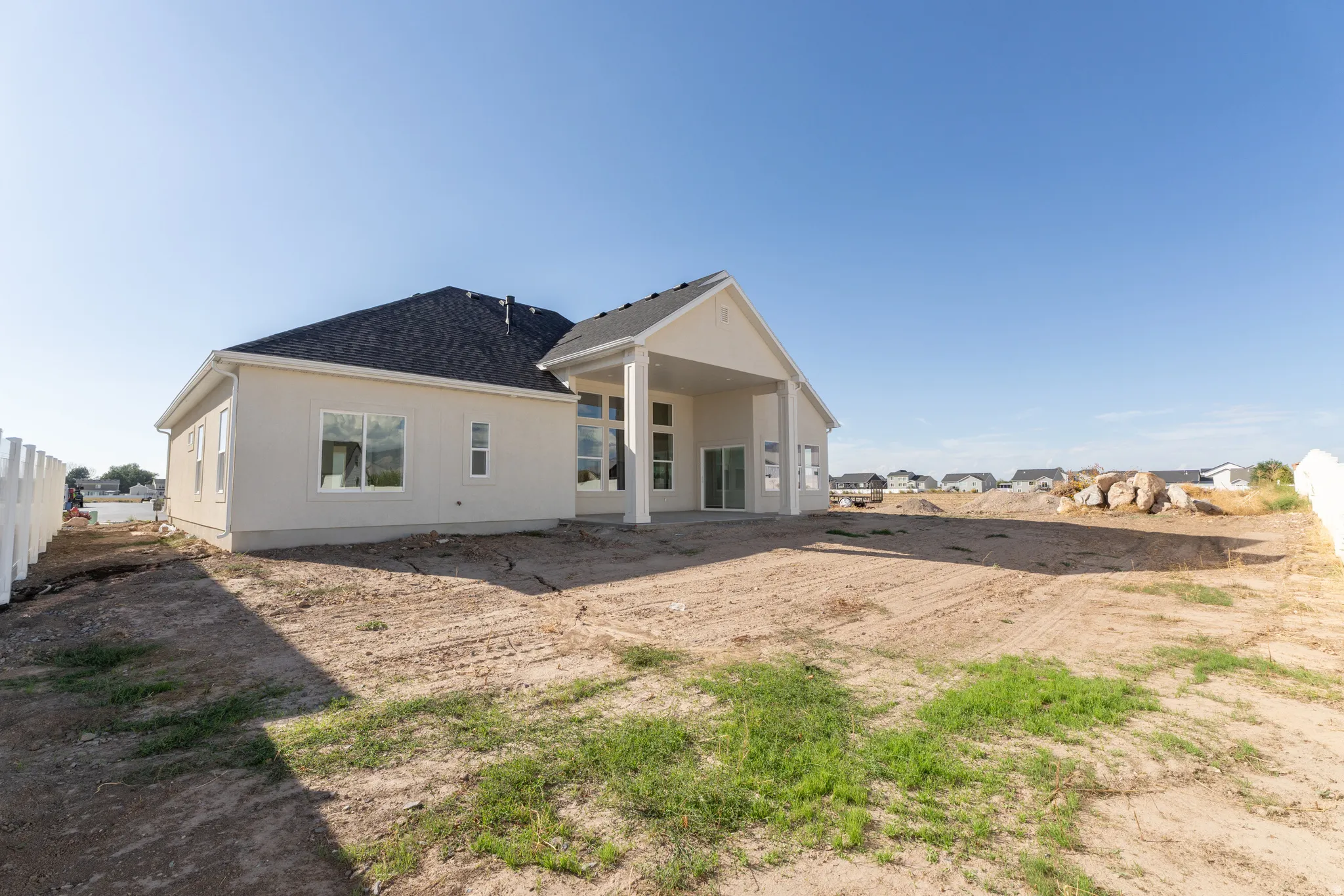 Spacious rear yard with a covered patio, multiple windows, and a dark shingle roof