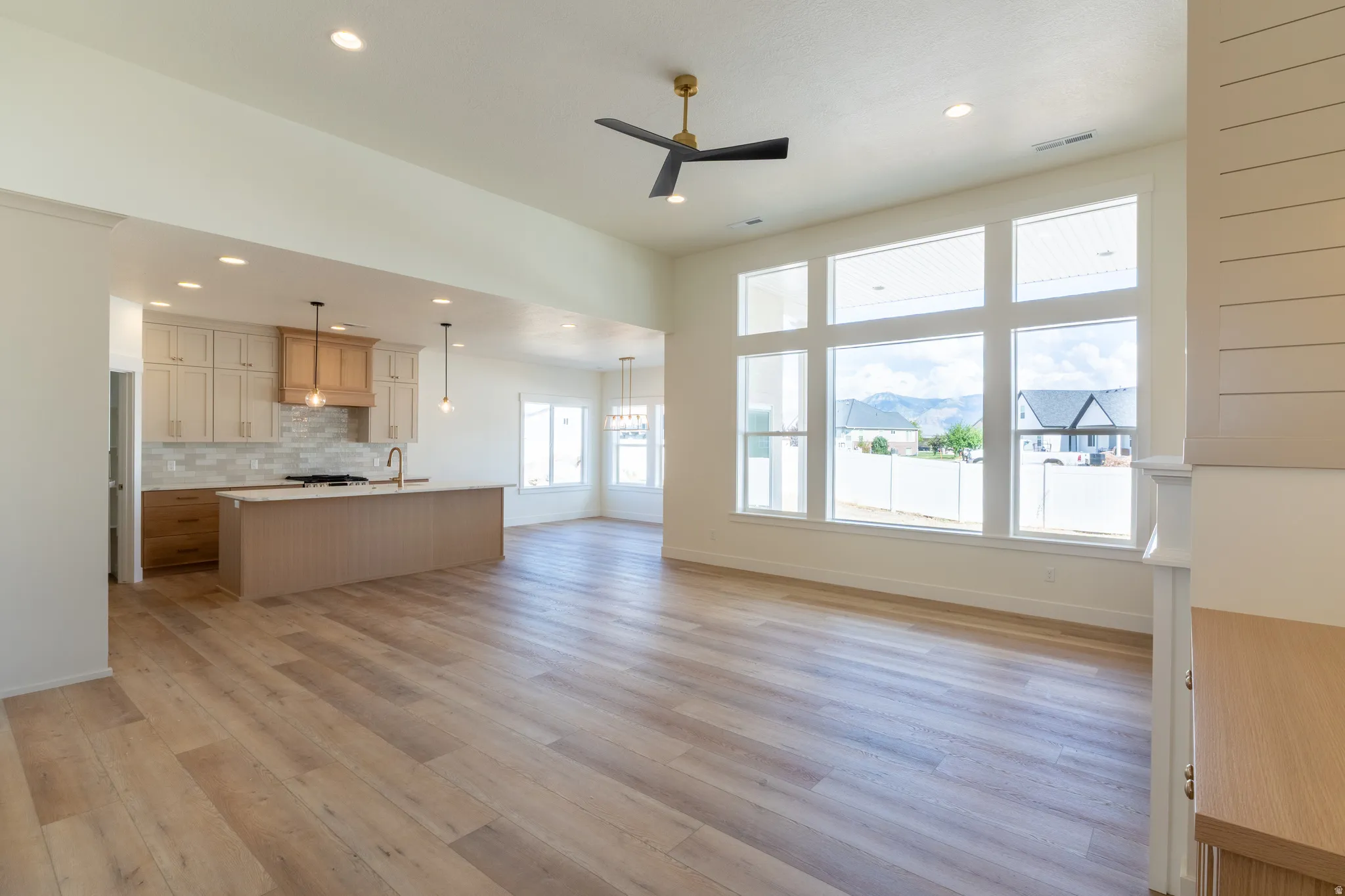 Expansive living area with wood-finish flooring, a contemporary ceiling fan, and large picture windows